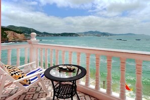 A balcony with a table and chairs, overlooking a coastal view with boats and mountains. - Haiyi Jiage Inn (Shengsi)