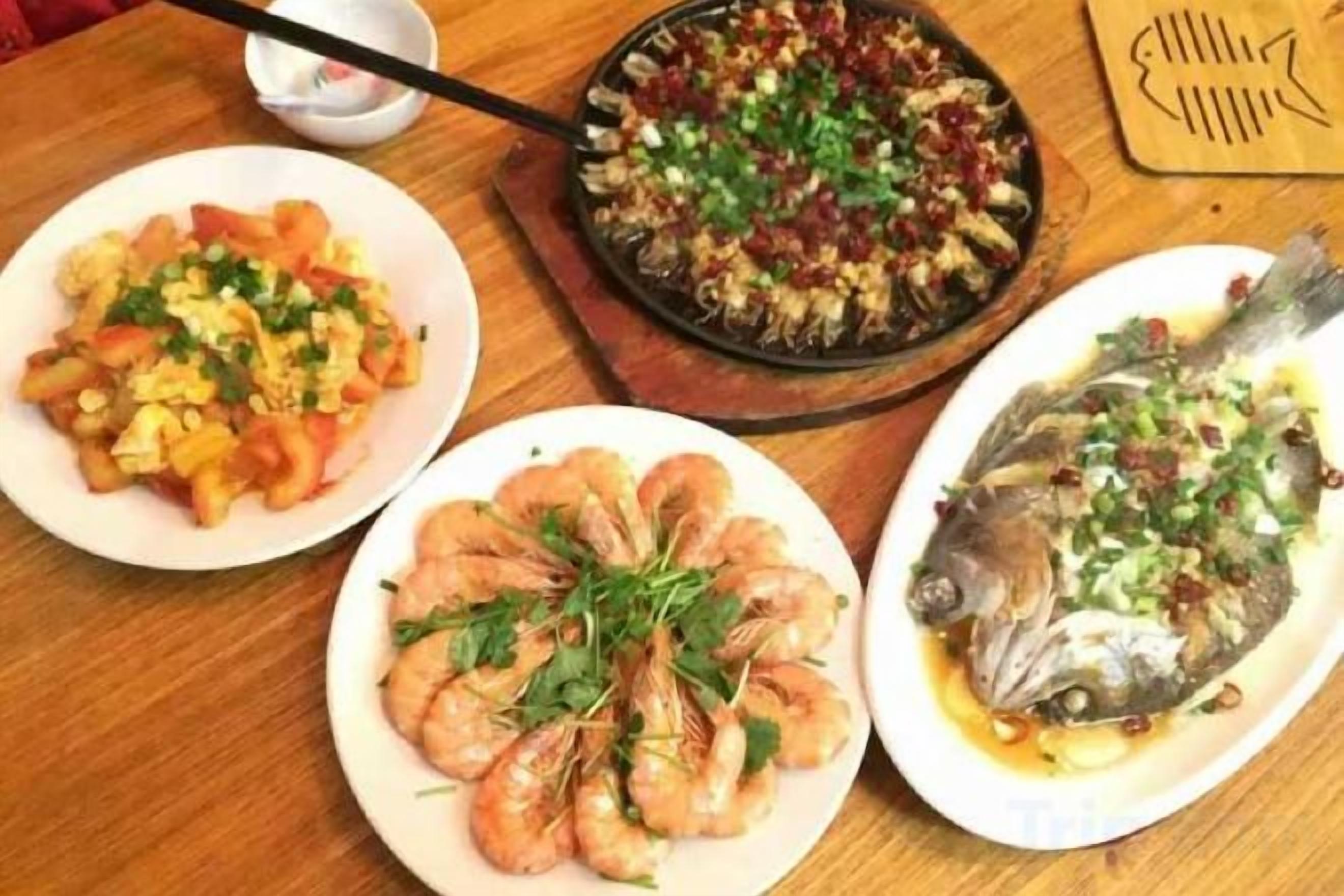 A wooden table with three plates of food, one with shrimp, one with a fish, and one with a mixed vegetable dish.