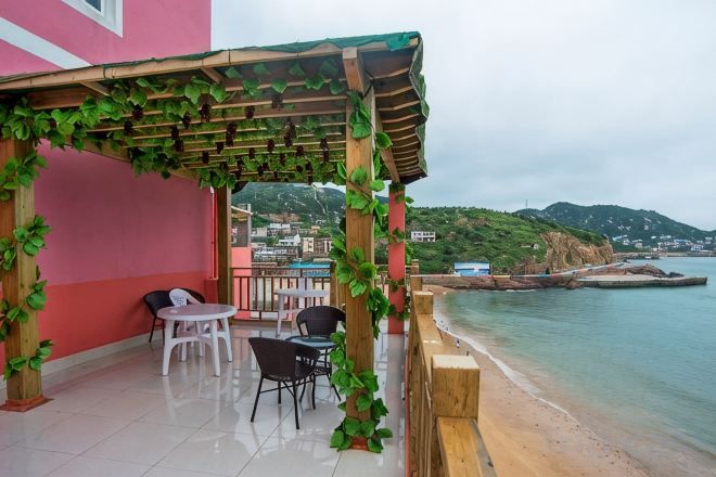 An outdoor seating area with a pergola, chairs, and a view of the sea and hills.