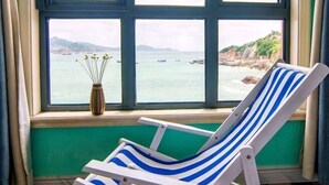 A room with a window view of a coastal area, a chair, and a vase with flowers. - Haiyi Jiage Inn (Shengsi)