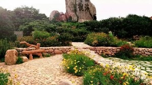 A garden with a stone pathway, large rock formations, and various plants. - Haiyi Jiage Inn (Shengsi)