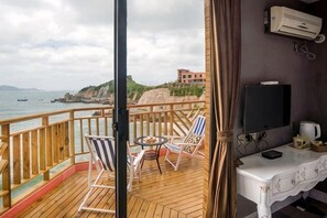 A balcony with a wooden floor, a table, two striped chairs, a TV, and an air conditioning unit.