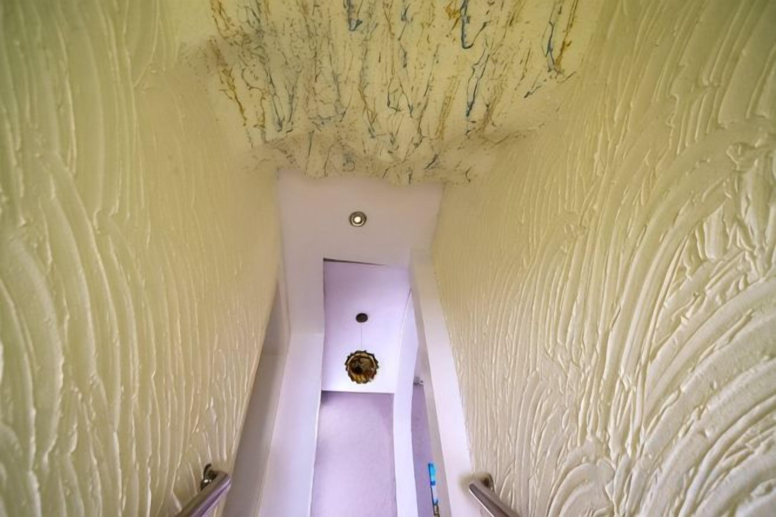 A narrow corridor with a white door at the end, leading to a room with a ceiling light fixture.