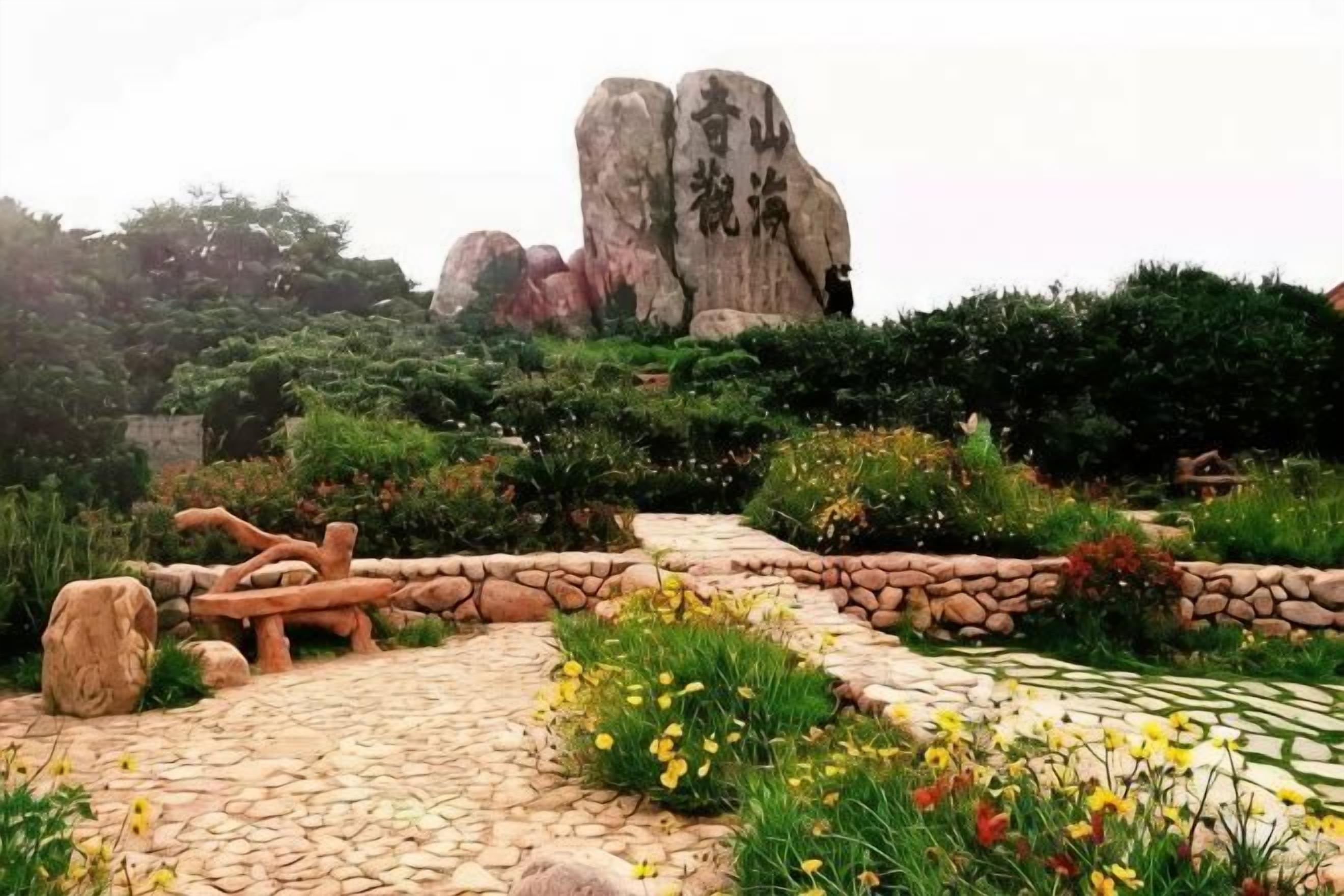 A garden with a stone pathway, large boulders, and various plants.
