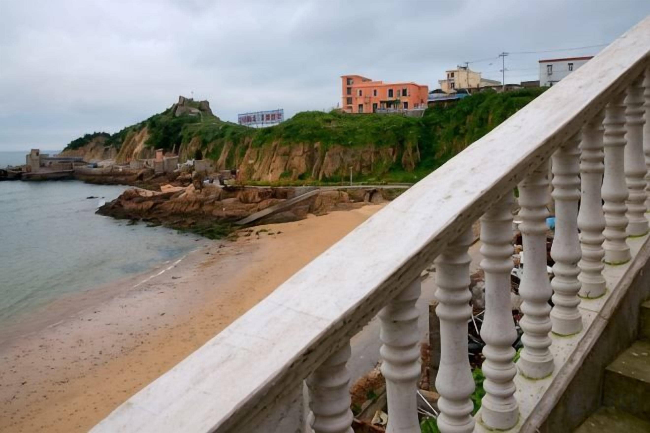 Une vue sur la côte, avec un escalier en pierre descendant vers une plage de sable, une côte rocheuse et des bâtiments situés sur une falaise.
