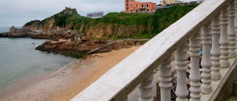A coastal view with a stone staircase leading down to a sandy beach, a rocky shoreline, and buildings on a cliff.