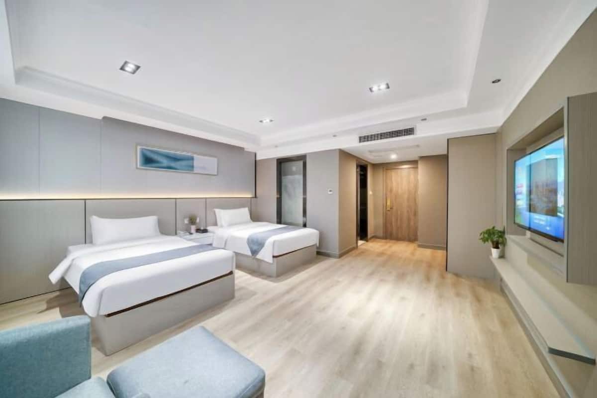Een moderne hotelkamer met twee bedden, een zithoek, een televisie en een groot raam.