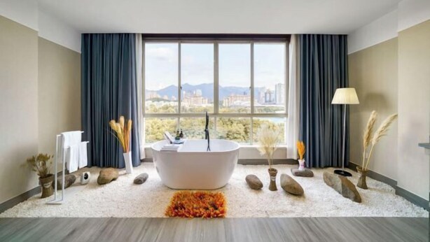 Een moderne badkamer met een vrijstaand bad, een groot raam met uitzicht op de stad, en decoratieve elementen zoals stenen en planten.