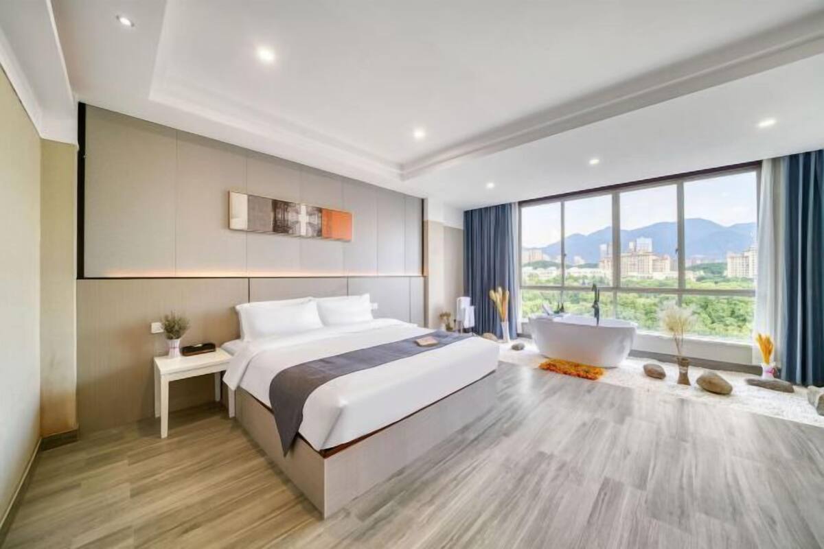 Een moderne hotelkamer met een groot bed, een badkuip en uitzicht over de stad.