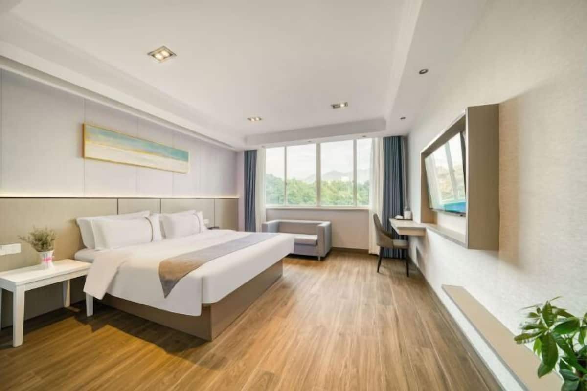 Een moderne hotelkamer met een groot bed, een bureau en een raam met uitzicht op groen.