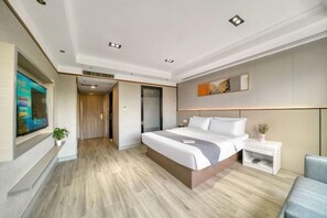 Quarto de hotel moderno com uma cama grande, televisão de tela plana na parede, mesa de cabeceira pequena com uma planta e piso de madeira.