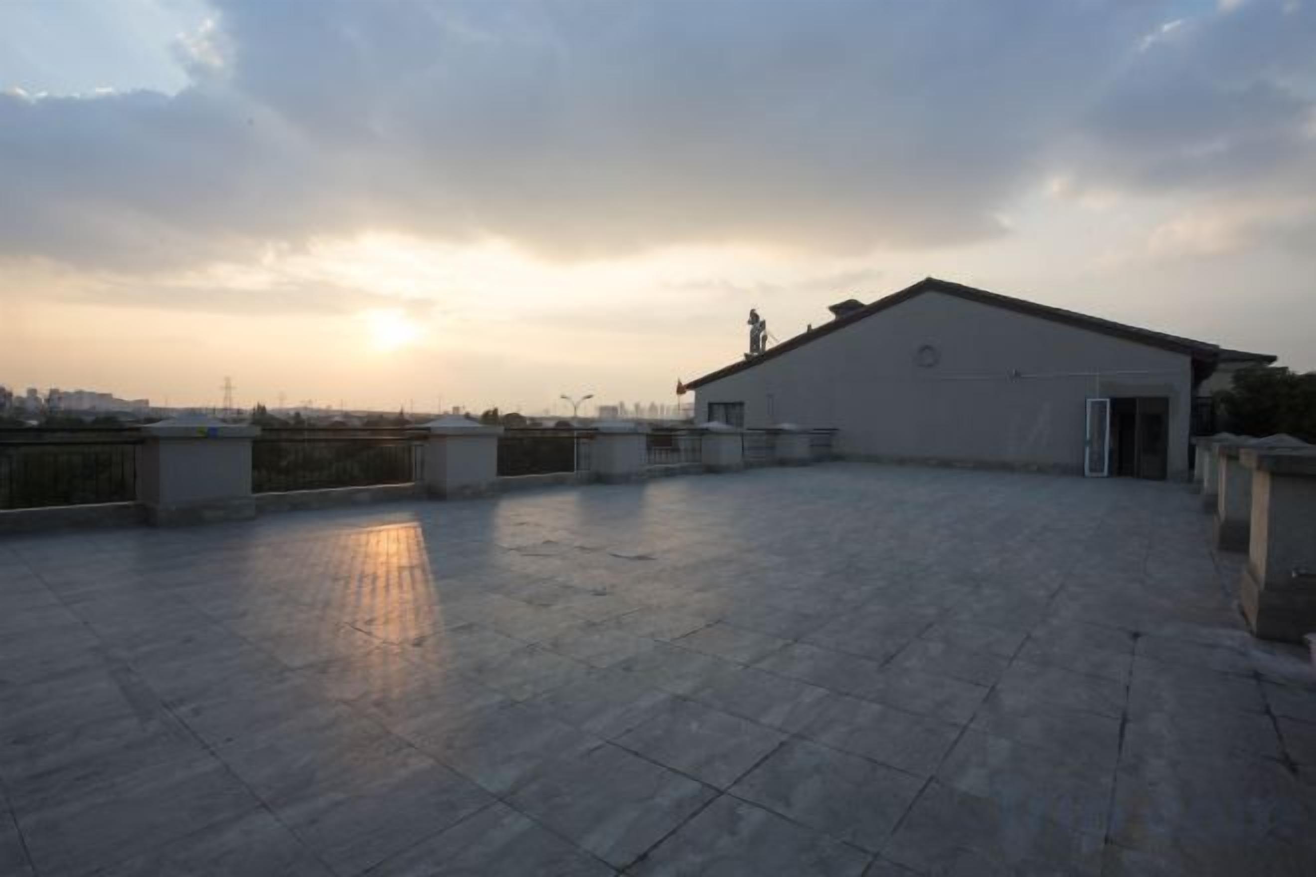 Una terraza en la azotea con un edificio al fondo, cielo despejado y un atardecer.