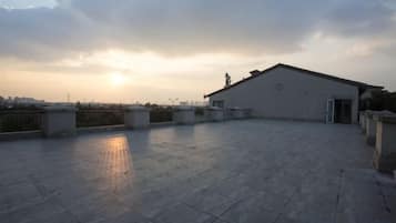 Una terraza en la azotea con un edificio al fondo, cielo despejado y un atardecer.