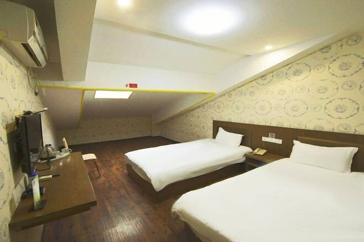 A hotel room with two single beds, a wooden desk, a flat-screen TV, and a patterned wallpaper.