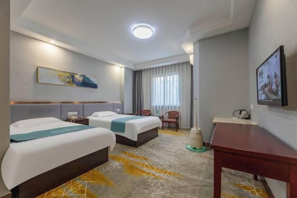 A hotel room with two beds, a desk, a chair, a TV, and a painting on the wall.