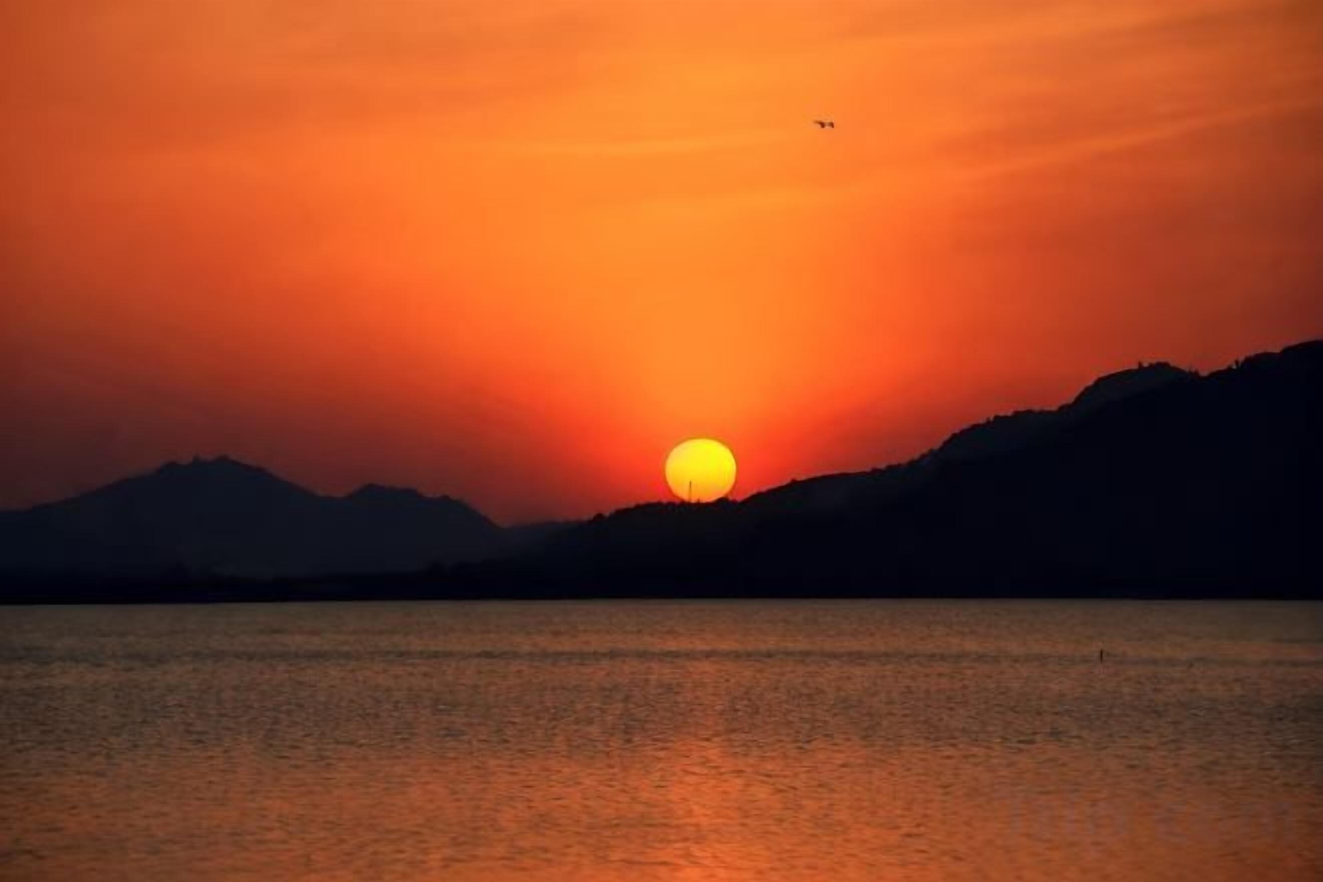 Un coucher de soleil sur une étendue d'eau, avec des montagnes en arrière-plan.