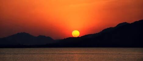 Un coucher de soleil sur une étendue d'eau, avec des montagnes en arrière-plan.