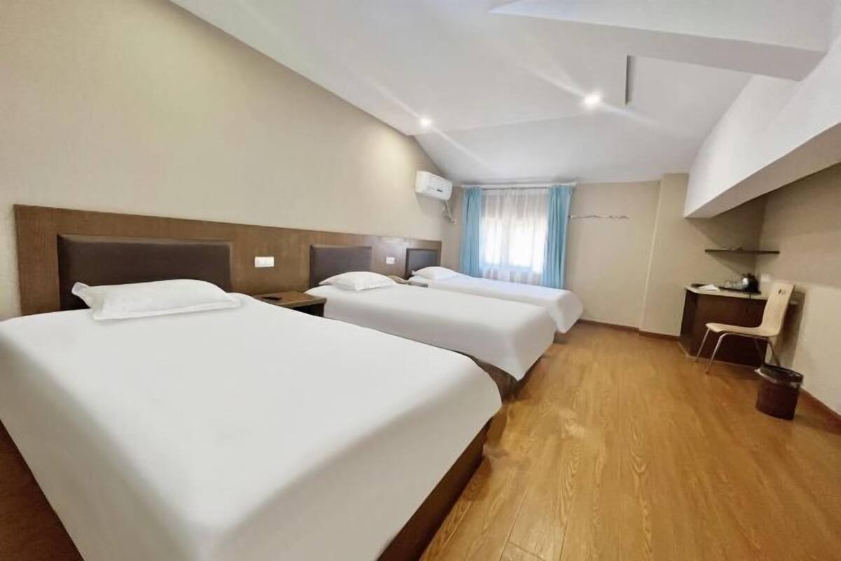 A hotel room with two beds, a desk, a chair, and a window with curtains.