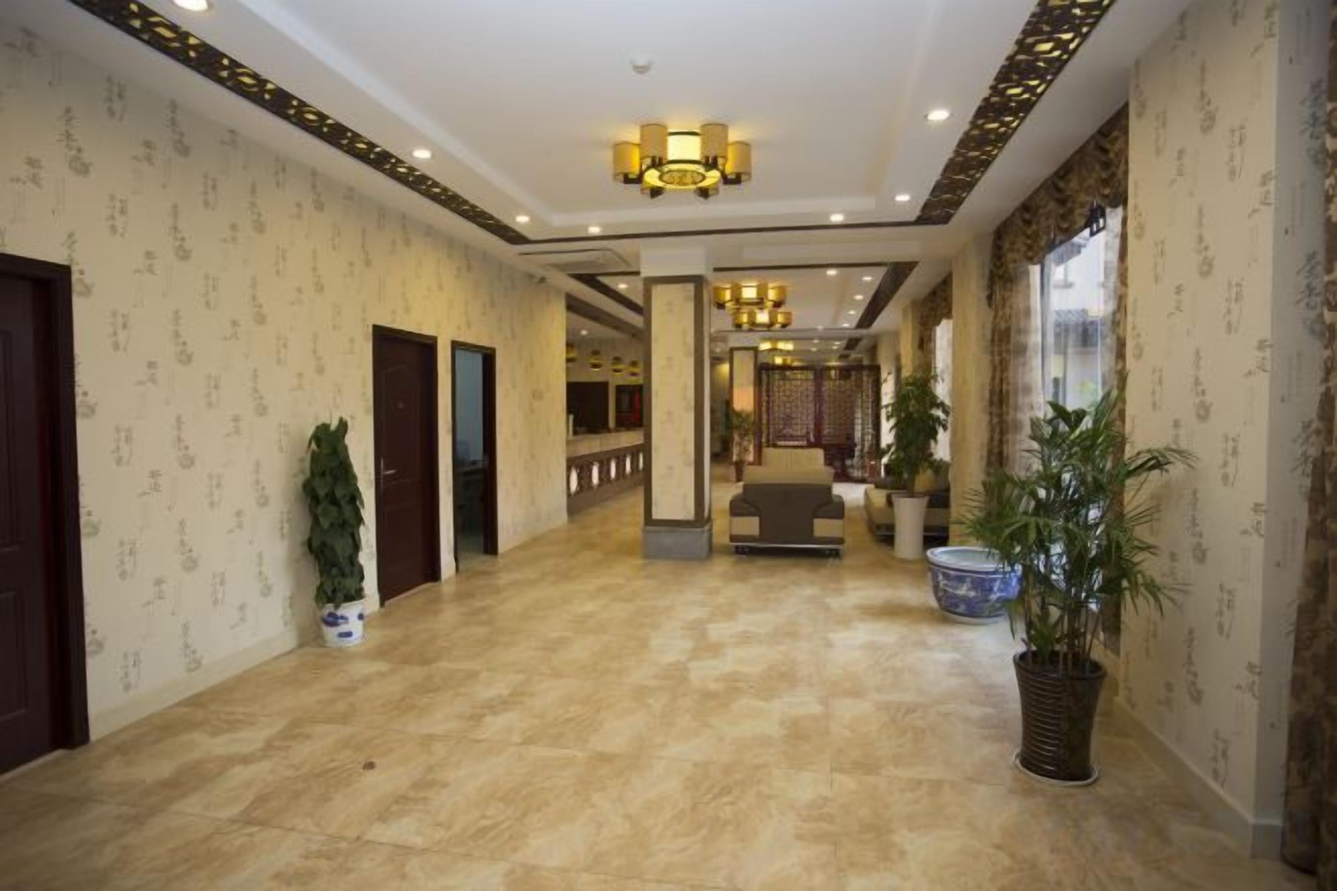A hotel lobby with a marble floor, a reception desk, and potted plants.