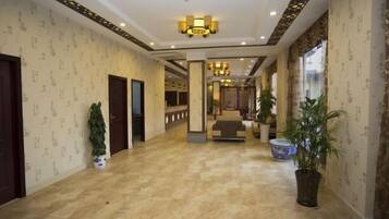 A hotel lobby with a marble floor, a reception desk, and potted plants.