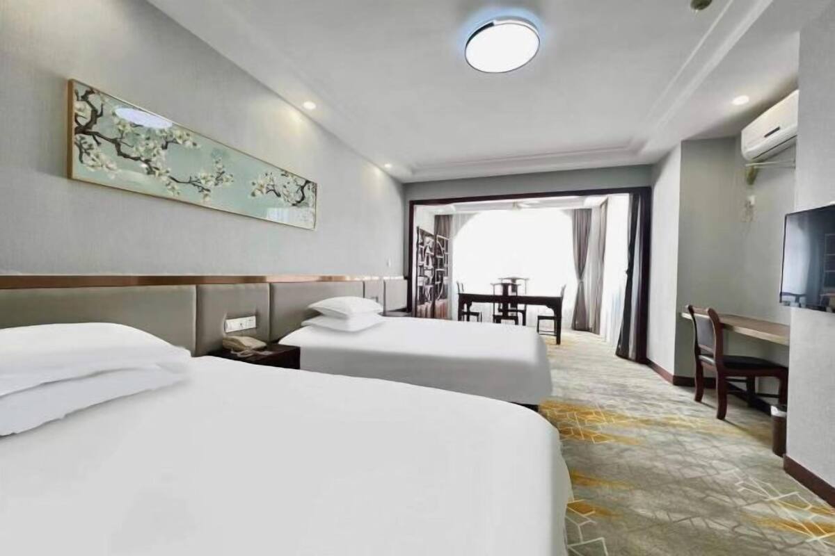 A hotel room with two beds, a desk, a chair, and a television.