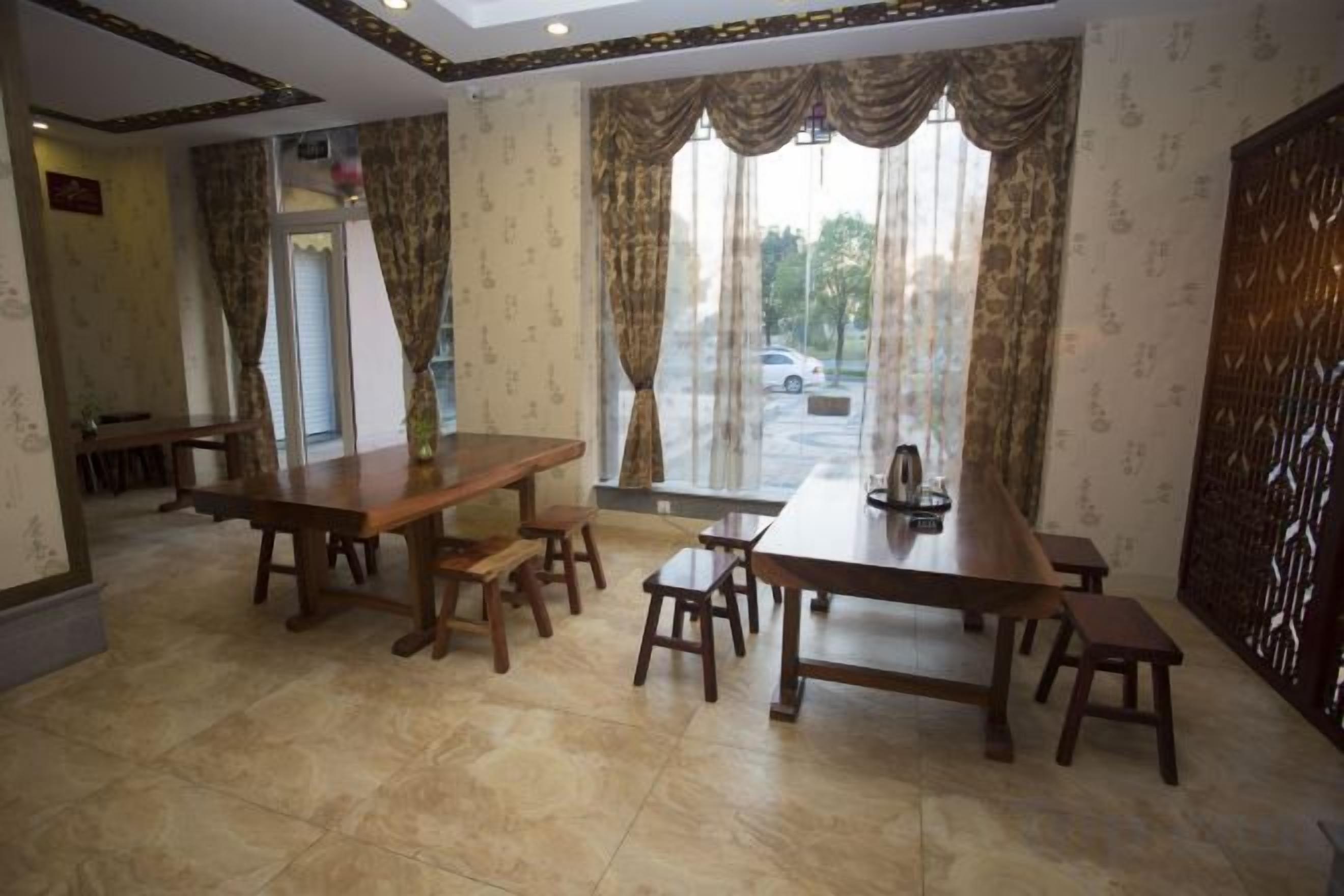 A dining area with a large wooden table and benches, a patterned wall, and a view through a window.