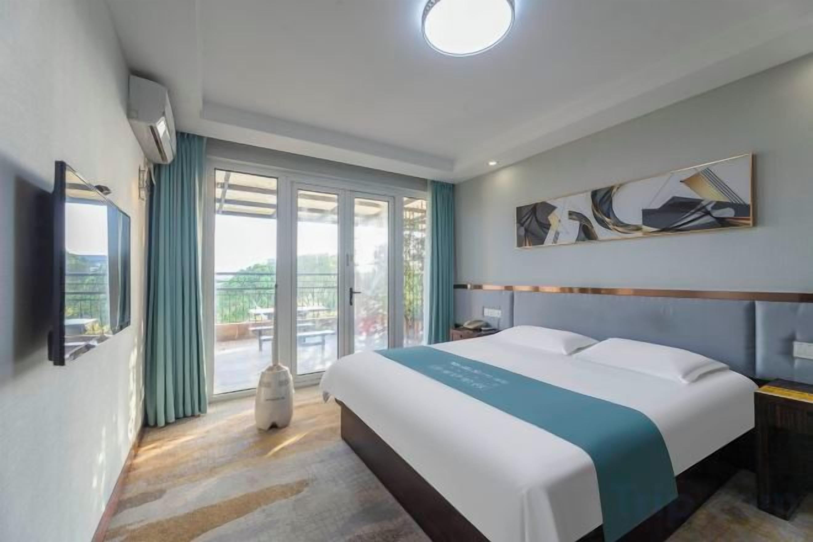 A hotel room with a bed, a flat-screen TV, a window with curtains, and a ceiling light.