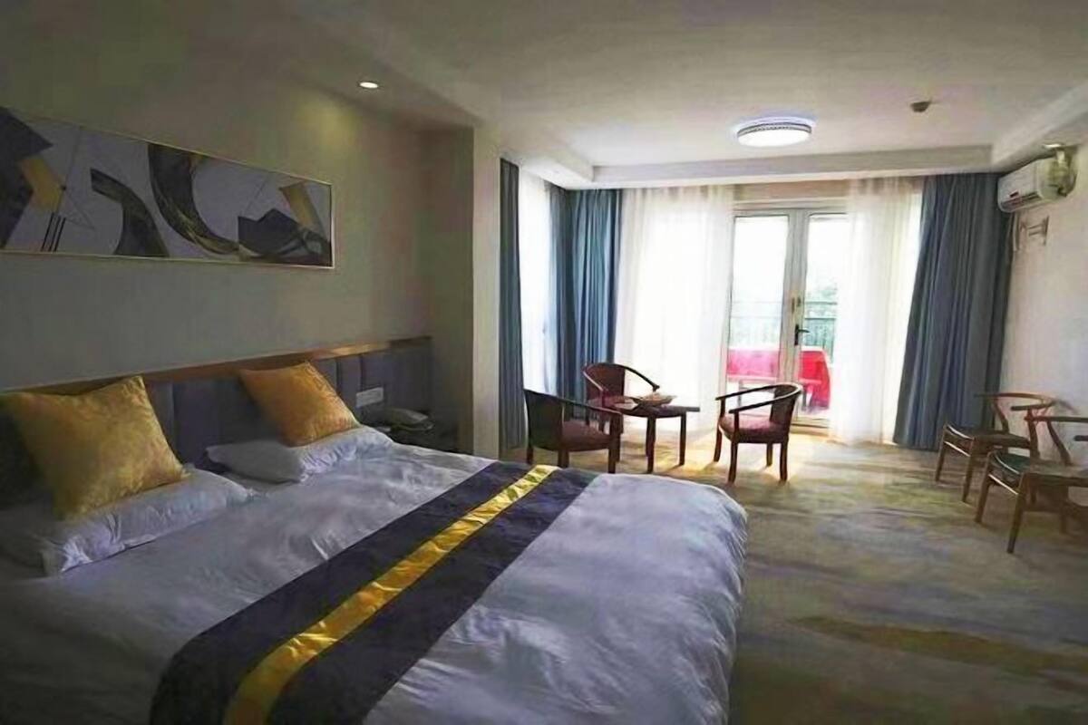 A hotel room with a large bed, a desk, and a chair. There is a window with curtains and a view of the outside.