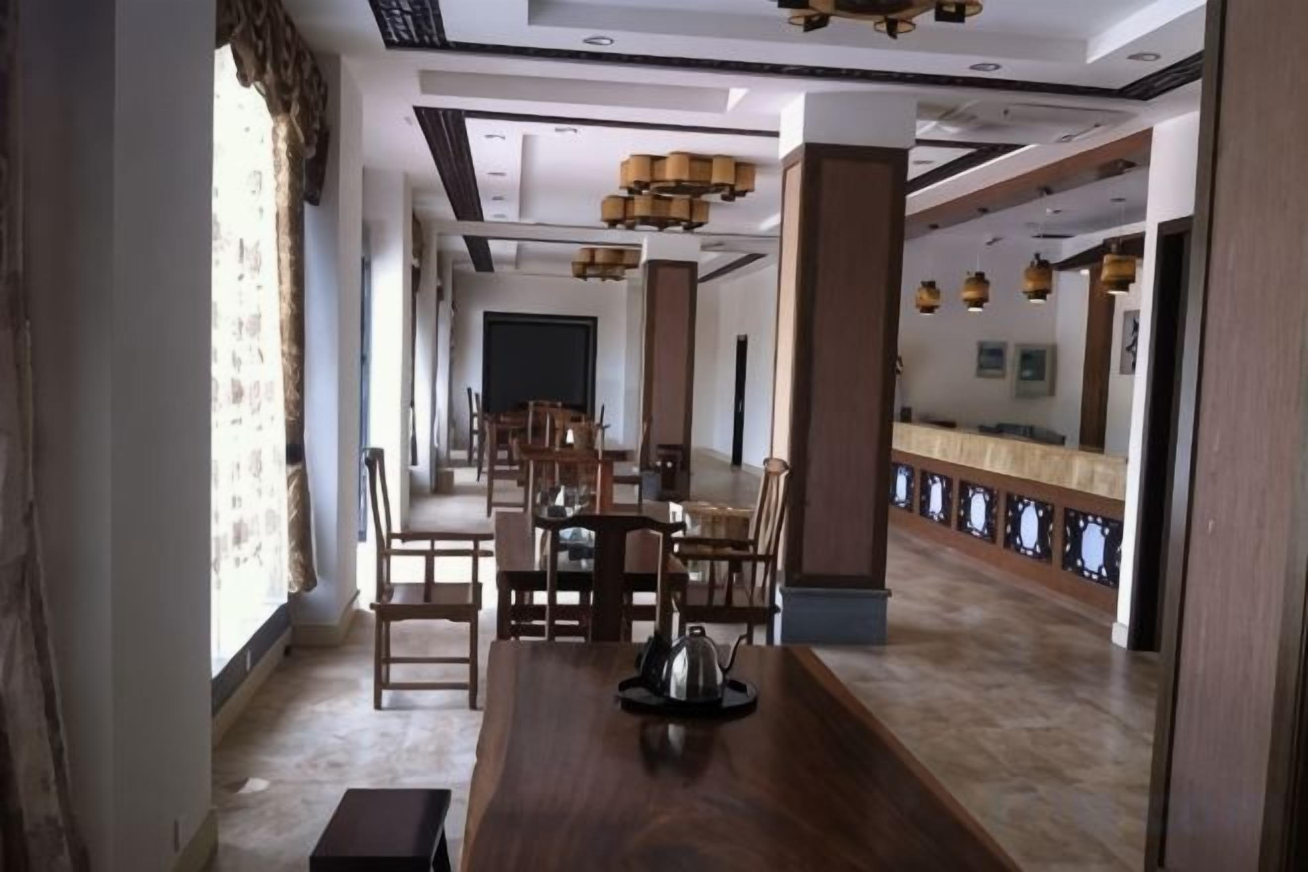 A hotel dining area with a long wooden table, multiple chairs, and a modern chandelier.