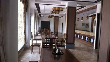 A hotel dining area with a long wooden table, multiple chairs, and a modern chandelier.