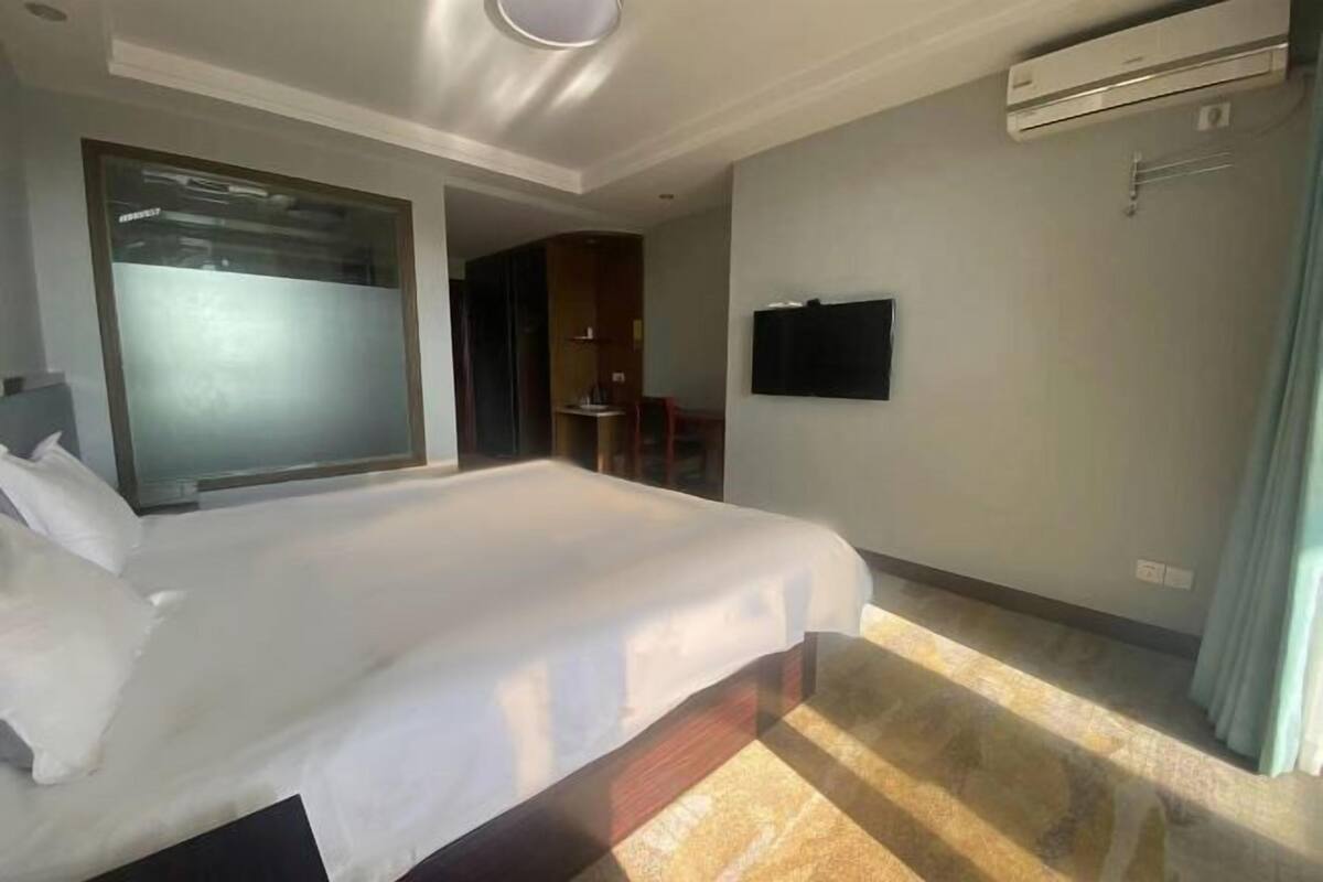 A hotel room with a large bed, a flat-screen TV mounted on the wall, and an air conditioning unit.