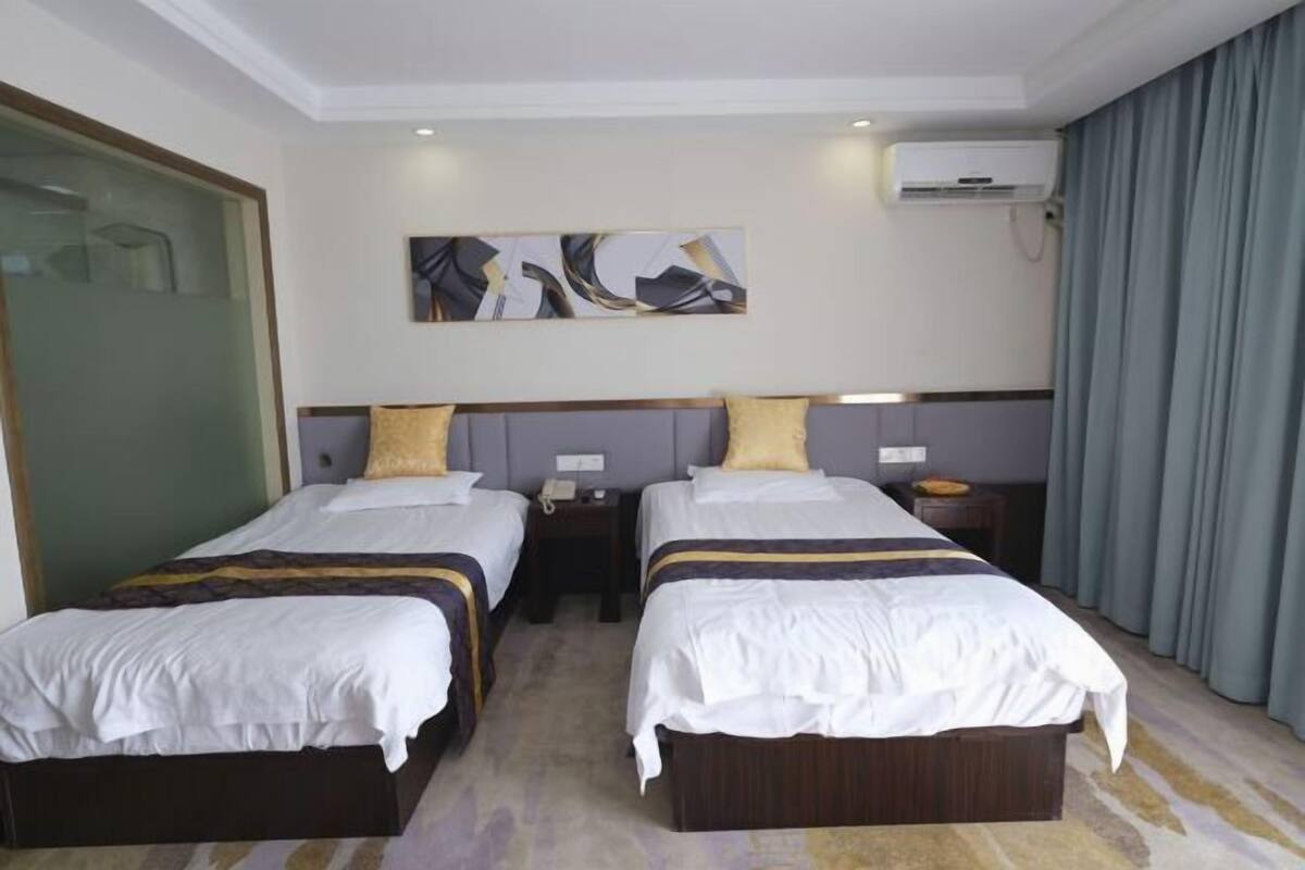 A hotel room with two beds, a large abstract painting on the wall, an air conditioning unit, and a curtain on the window.