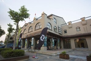 A building with a traditional architectural style, featuring arched windows and a tiled roof. There are outdoor seating areas and a small garden with a potted plant. - Chamagudao Hotel (Ningbo)