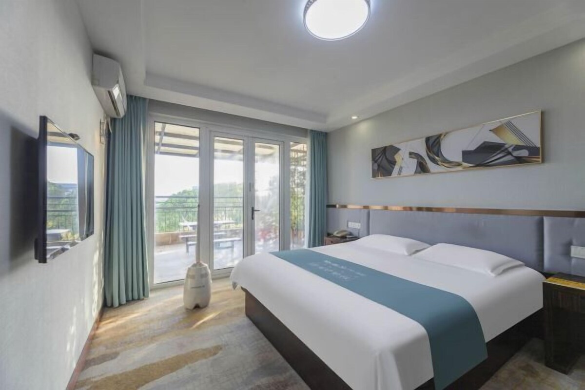 Ein Hotelzimmer mit Bett, Flachbildfernseher, großem Fenster mit Vorhängen und Deckenleuchte.