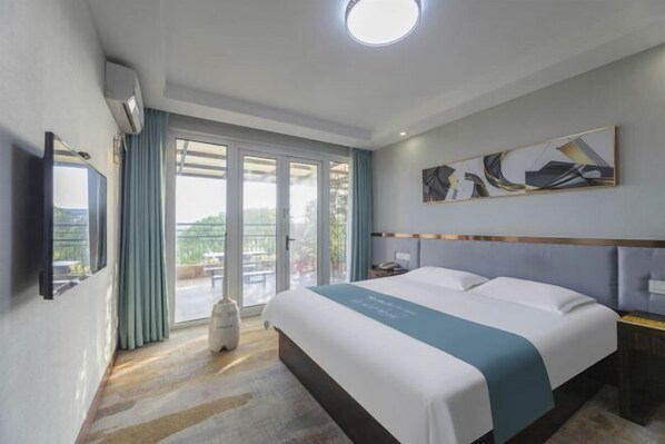 Ein Hotelzimmer mit Bett, Flachbildfernseher, großem Fenster mit Vorhängen und Deckenleuchte.