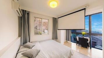 A bedroom with a bed, a projector screen, and a balcony with a table and chairs.