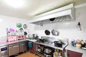 A commercial kitchen with stainless steel appliances, a ventilation hood, and various cooking utensils. - Hongfu Inn (Zhoushan)