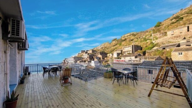 A wooden deck with outdoor seating and a view of a hillside town. - Hongfu Inn (Zhoushan)