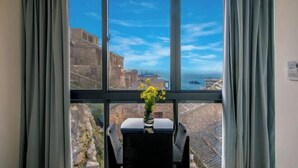 A room with a large window, a small table with a vase of flowers, and a view of a historic building and the sea. - Hongfu Inn (Zhoushan)
