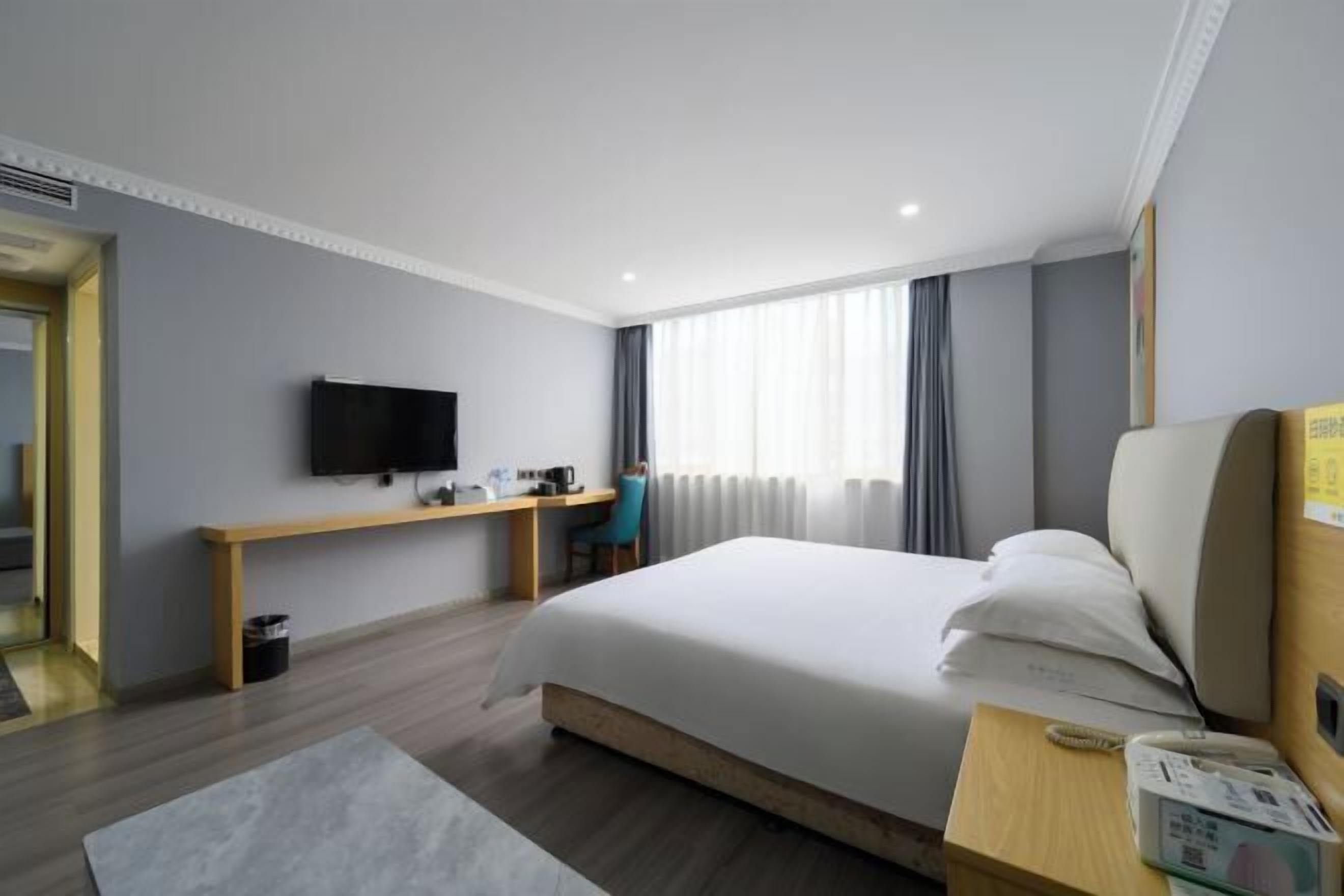 Una habitación de hotel con cama, escritorio, televisor y ventana con cortinas.