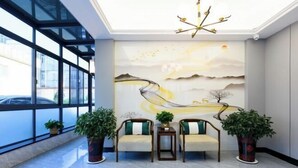 A lobby with a modern design, featuring a large window, a reception desk, and two sofas with green cushions. - Xianggang Hudie Hotel (Anqing)
