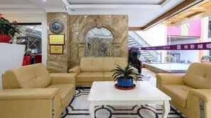 A lobby with beige sofas, a white coffee table, and a marble wall with a framed certificate. - Xianggang Hudie Hotel (Anqing)