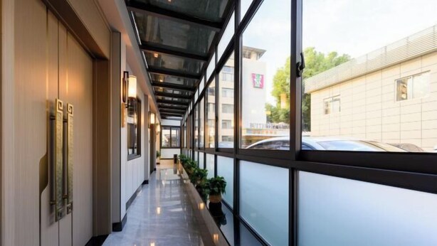 A corridor with a glass wall, potted plants, and a reflective floor. - Xianggang Hudie Hotel (Anqing)
