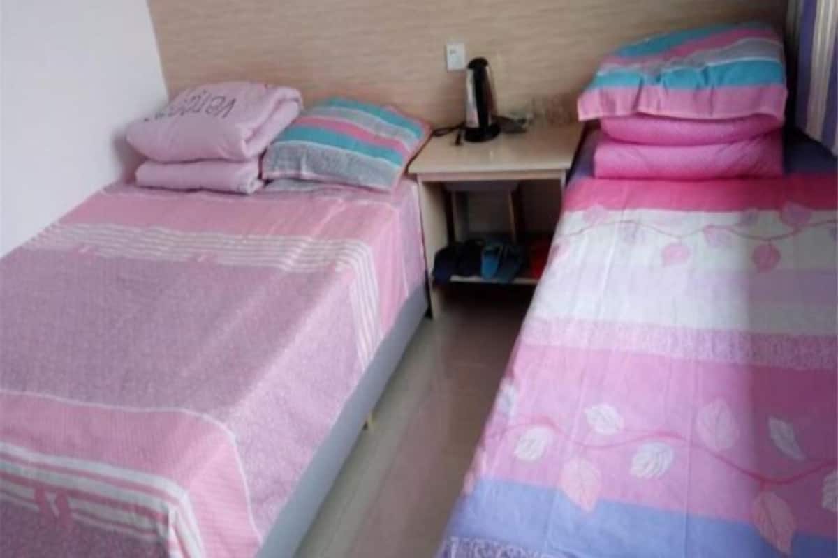 Una habitación con dos camas individuales, cada una con una colcha a rayas rosada y blanca. Hay una mesita con un objeto negro encima, posiblemente un teléfono o un control remoto.