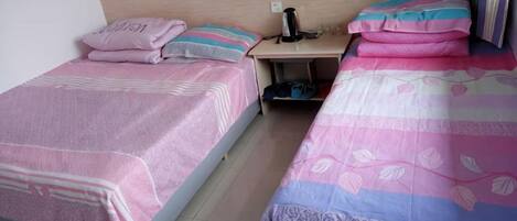 Two single beds with pink and blue floral bedding, a wooden headboard, and a nightstand with a black object.