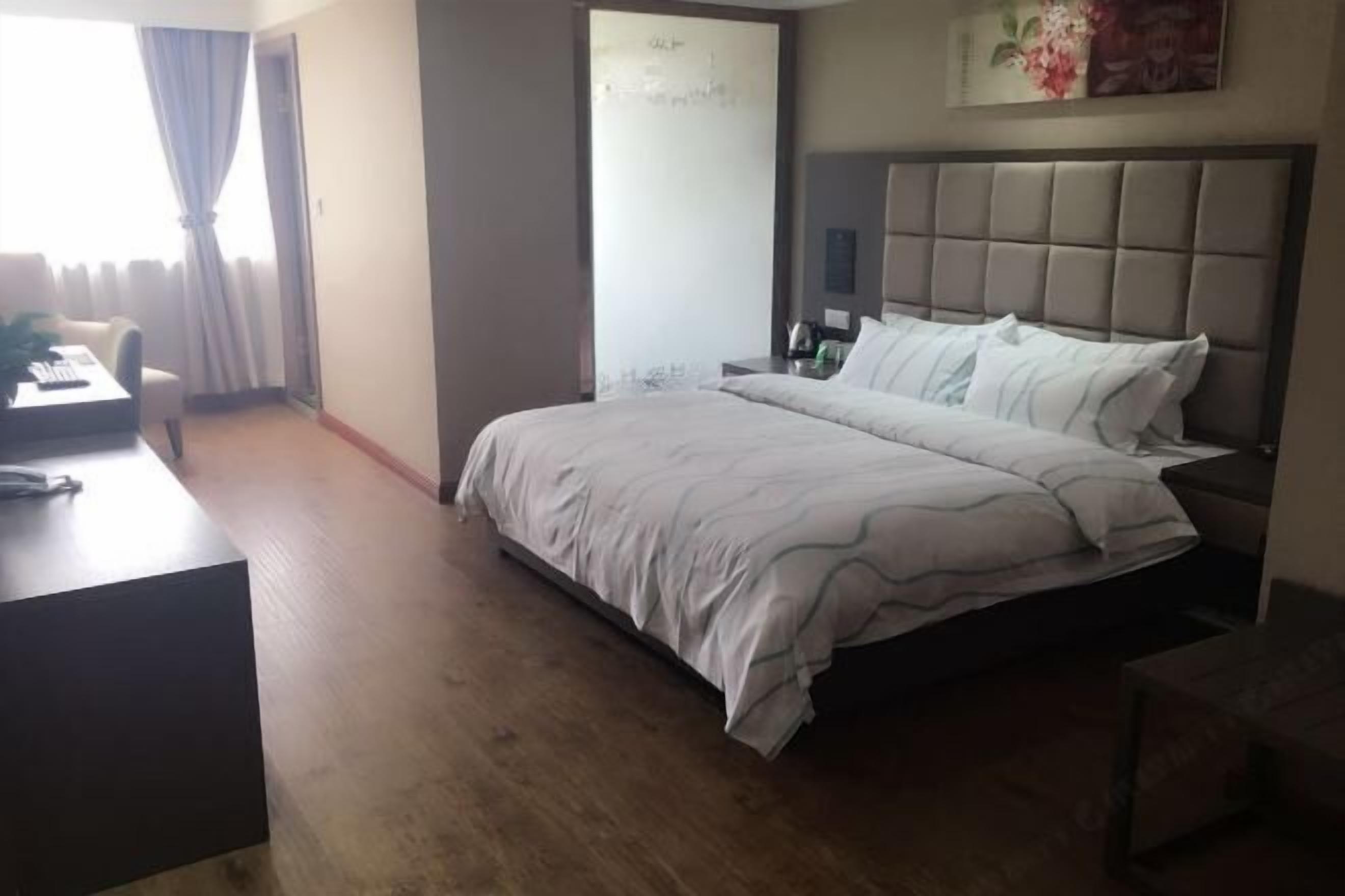 A hotel room with a bed, a desk, a chair, a nightstand, and a window with curtains.