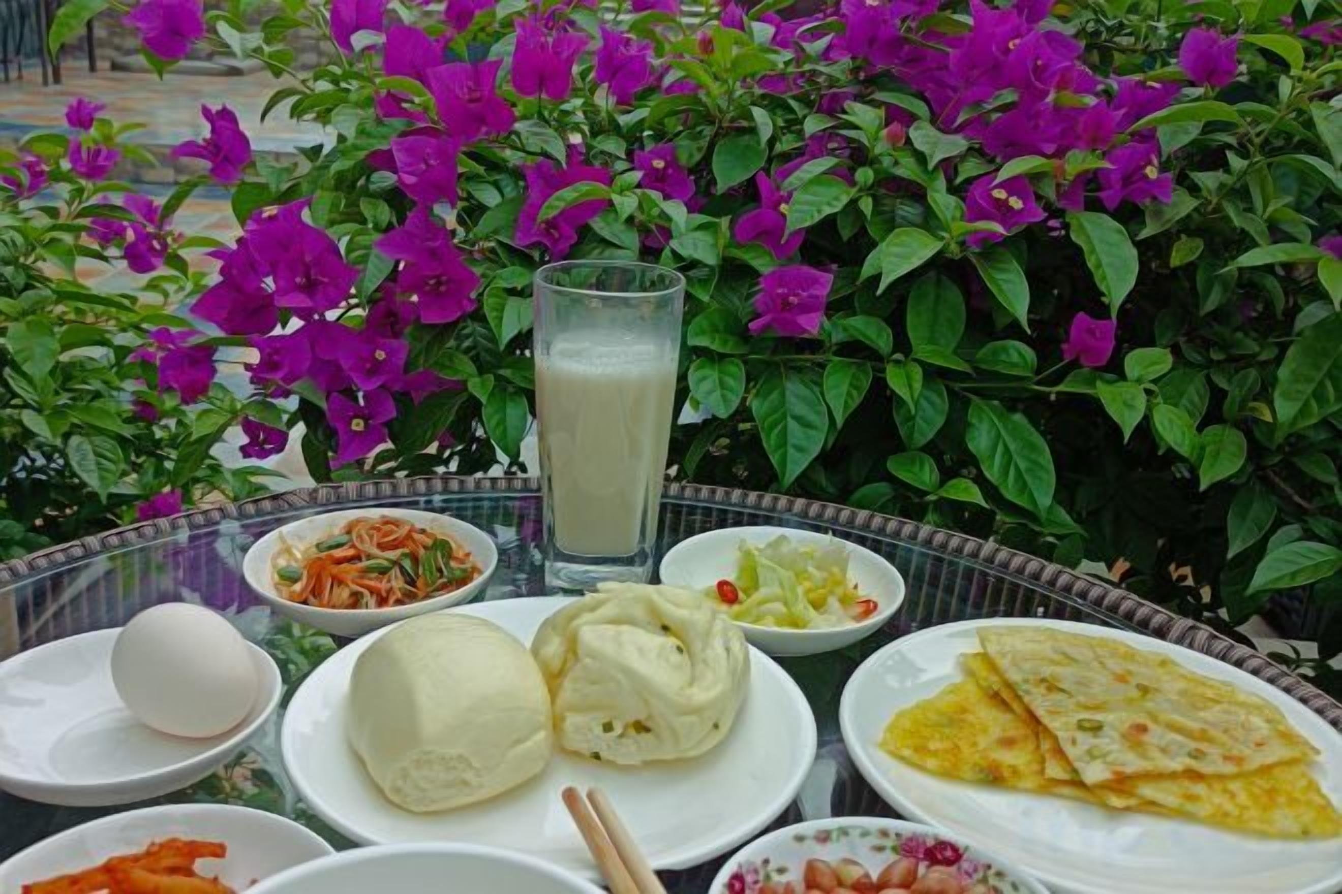 Una mesa con alimentos, incluyendo un vaso de una bebida clara, platos de comida y un bol de verduras.
