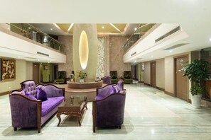 A lobby with a reception desk, two purple sofas, a coffee table, and a large decorative pillar. - Olive Tree Hotel(Xuhai Times Jianyang Middle School Square) (Jianyang)