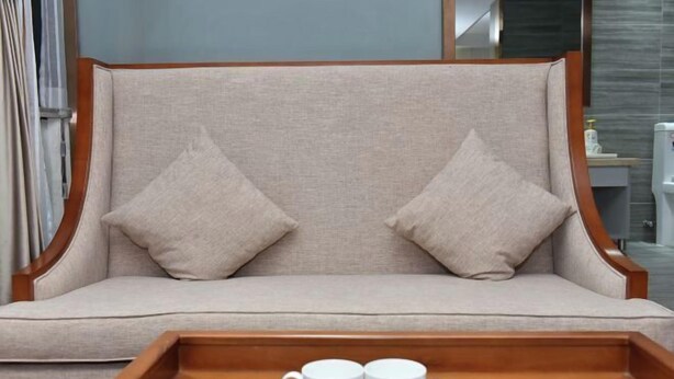 A beige sofa with two pillows, a wooden tray with two white mugs, and a glass bowl. - Olive Tree Hotel(Xuhai Times Jianyang Middle School Square) (Jianyang)