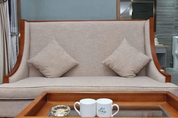 A beige sofa with two pillows, a wooden tray with two white mugs, and a glass bowl. - Olive Tree Hotel(Xuhai Times Jianyang Middle School Square) (Jianyang)
